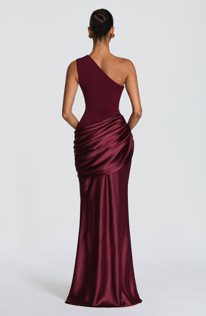 Robe longue prune devant un mur clair, mannequin un bras relevé derrière la tête, drapé satiné marqué. 18