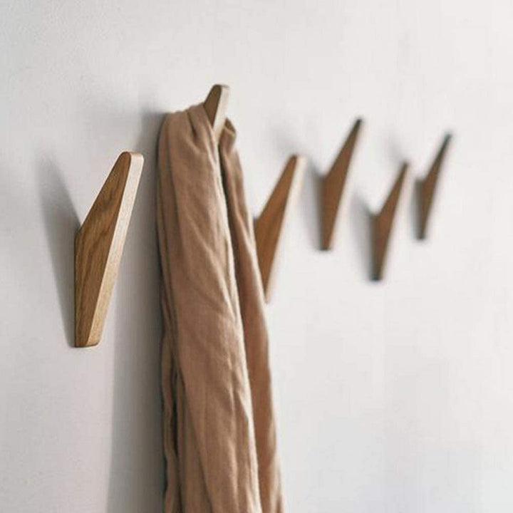 Rangée de crochets en bois fixés au mur blanc, une écharpe beige drapée sur l'un d'eux, vue en perspective. 2