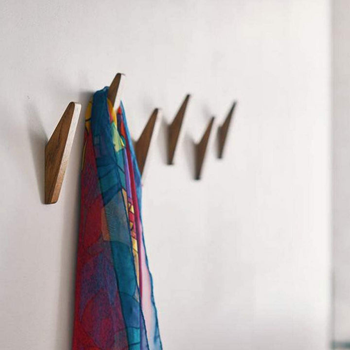 Crochets en bois foncé alignés sur un mur blanc, avec une écharpe colorée rouge, bleue et jaune suspendue au premier. 3