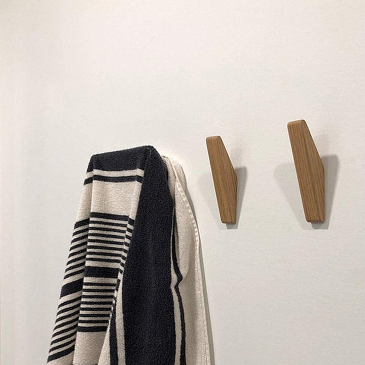 Deux crochets en bois posés sur un mur blanc, à côté d'une serviette rayée noire et blanche accrochée à un troisième. 4