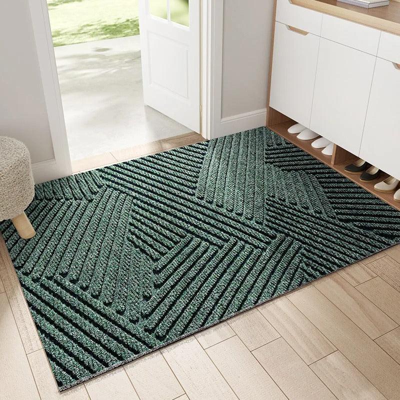 Paillasson vert foncé à rayures en relief formant des triangles géométriques, posé dans une entrée devant un meuble à chaussures. 1
