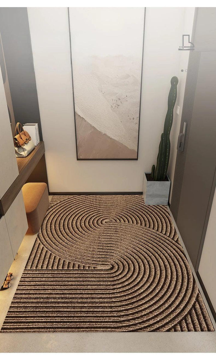 Paillasson brun à grands cercles concentriques en relief, posé dans un couloir d'entrée moderne avec cactus, tableau et pouf. 6