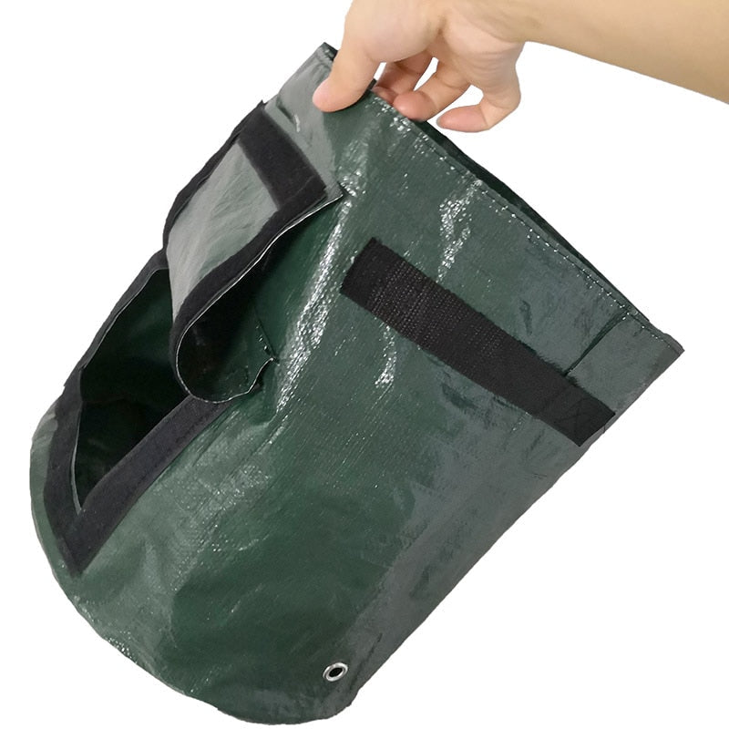 Sac de culture vert tenu à la main, rabat de récolte relevé, poignée en sangle noire et œillet de drainage visible en bas. 6