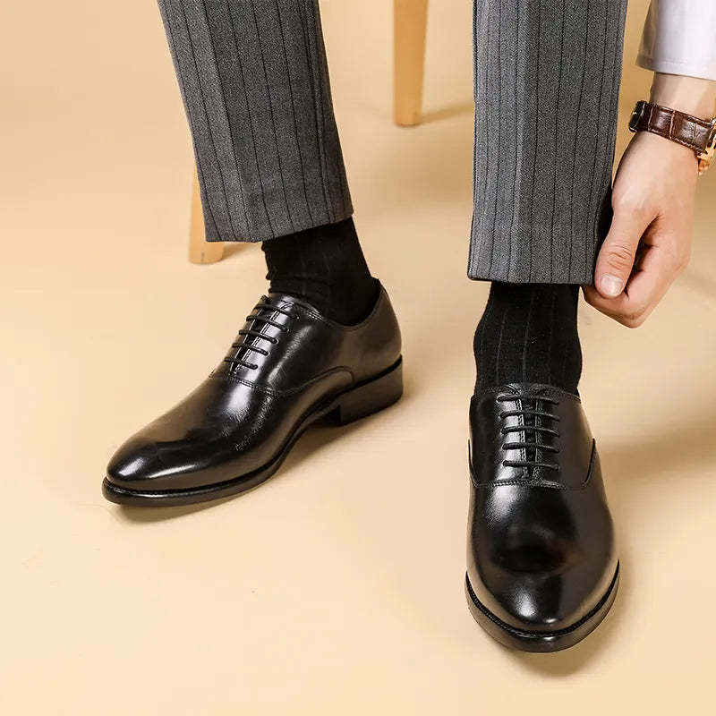 Oxford noires en cuir brillant portées avec un pantalon gris rayé, un homme ajustant son revers 1