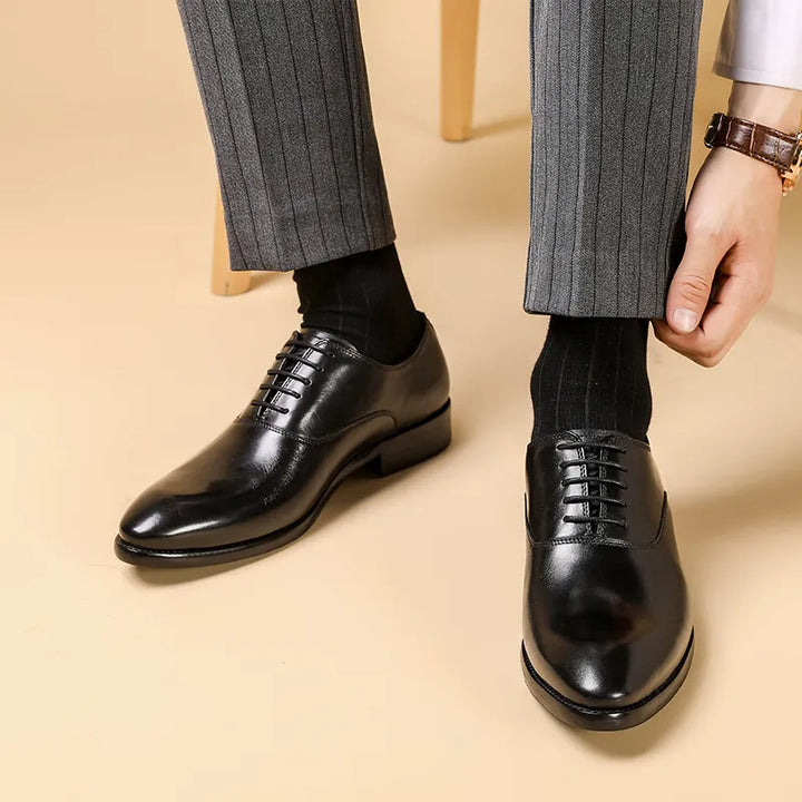 Oxford noires en cuir brillant portées avec un pantalon gris rayé, un homme ajustant son revers 1