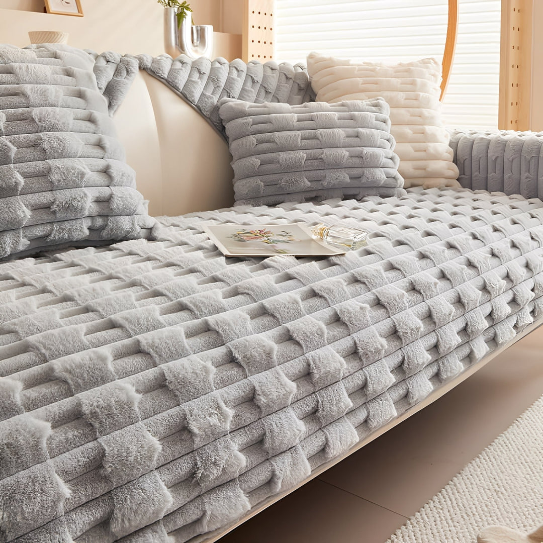 Housse peluche coloris gris clair sur le canapé, avec coussins assortis et coussin crème, livre et flacon sur l'assise. 10