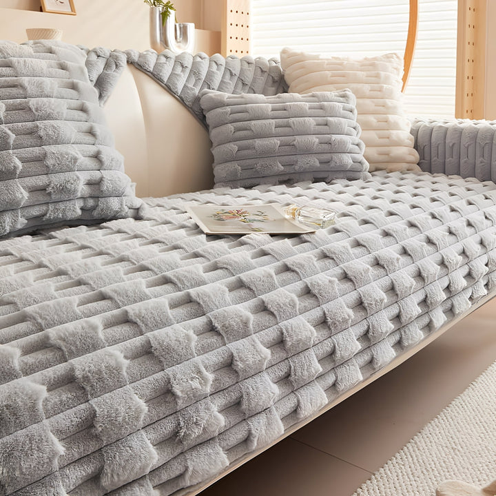 Housse peluche coloris gris clair sur le canapé, avec coussins assortis et coussin crème, livre et flacon sur l'assise. 10