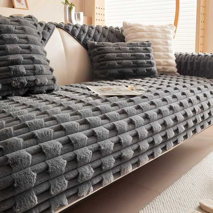 Housse peluche coloris gris foncé sur le canapé, avec coussins assortis et un coussin crème, livre et flacon sur l'assise. 11