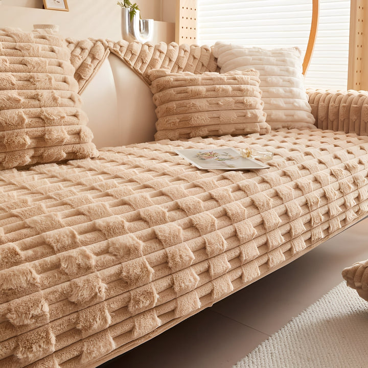 Housse peluche coloris beige camel sur le canapé, avec coussins assortis, livre et petit flacon posés sur l'assise. 9