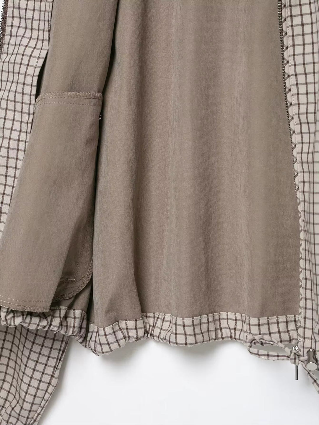 Veste ouverte à plat montrant la doublure unie beige-gris, une poche intérieure et l'ourlet à carreaux avec cordon de serrage. 5