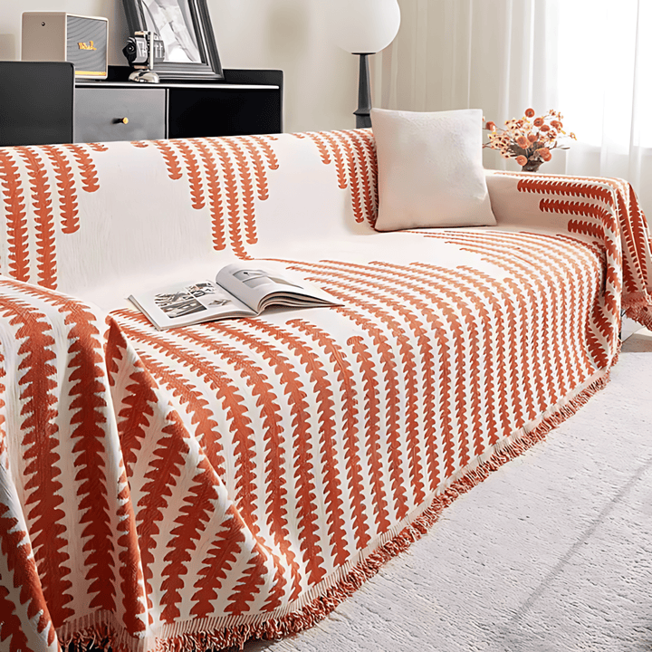Version orange et crème de la housse sur un canapé, avec magazine ouvert, coussin blanc et franges. 7