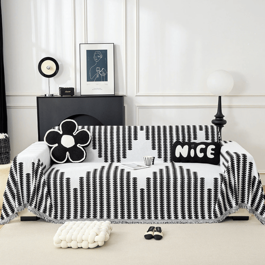 Vue de face d'un canapé recouvert de la housse noir et blanc à motifs de feuilles, avec coussins fleur et rectangulaire. 1