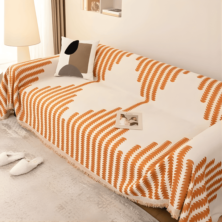 Vue en plongée d'un canapé couvert de la housse crème à motifs de feuilles orange et franges. 4