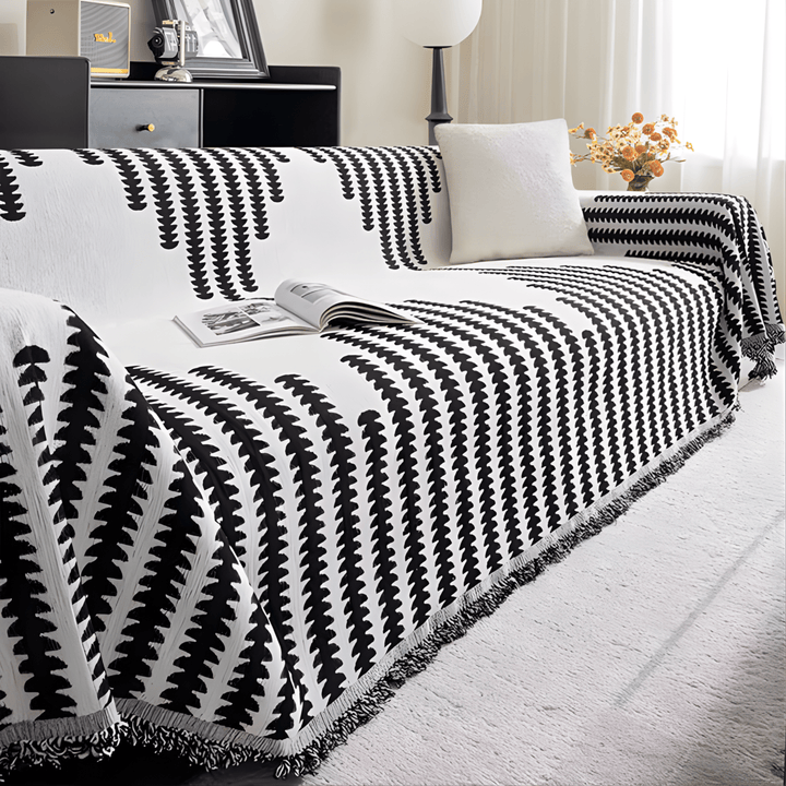 Housse noir et blanc posée sur un canapé d'angle, avec magazine ouvert, coussin blanc et franges visibles. 6