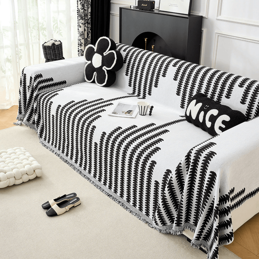 Vue en perspective de la housse noir et blanc sur un canapé, avec coussins décoratifs et franges au bord. 5