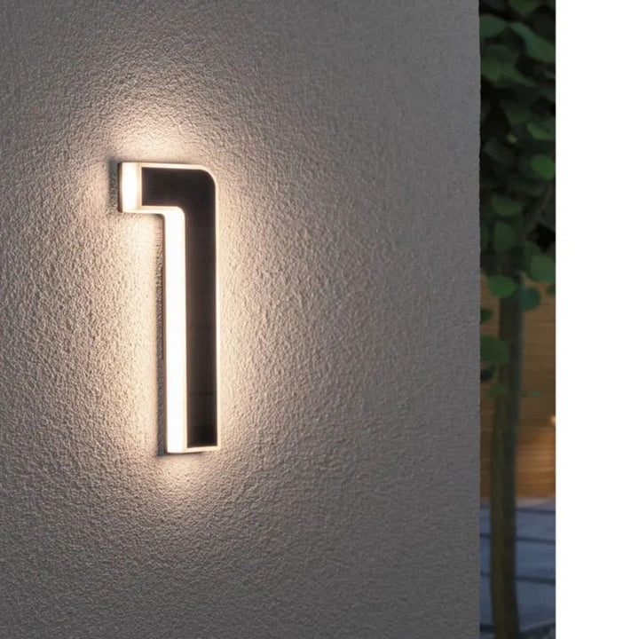 Chiffre 1 éclairé sur un mur de crépi gris, face solaire sombre et contour diffusant une lumière chaude. 2