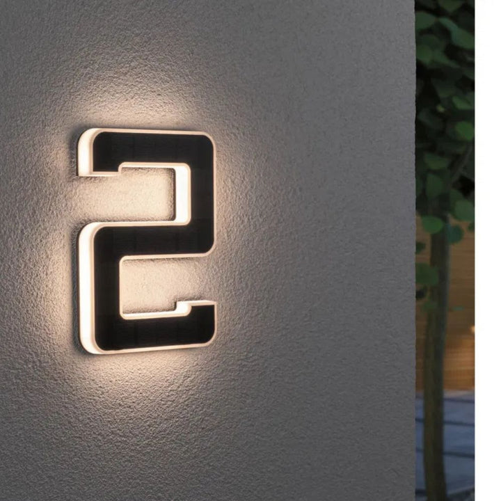 Chiffre 2 lumineux fixé au mur crépi, surface solaire noire entourée d'un liseré de lumière blanc chaud. 3