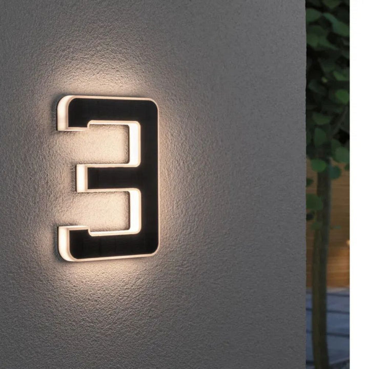 Chiffre 3 éclairé de nuit sur un mur gris texturé, avec panneau solaire noir et lumière douce sur le pourtour. 4