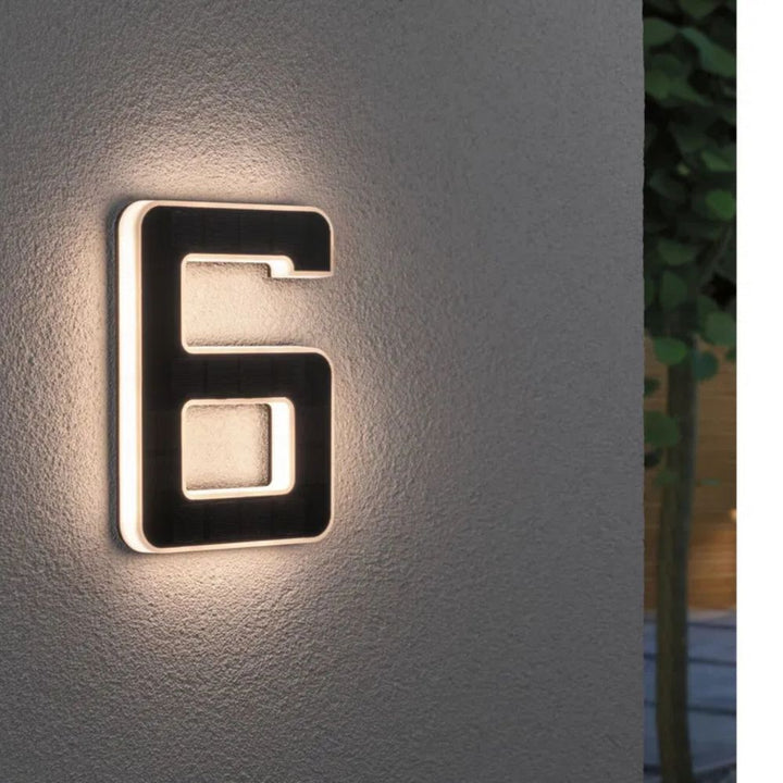 Chiffre 6 lumineux sur un mur de crépi gris, face solaire sombre et halo de lumière blanc chaud. 7