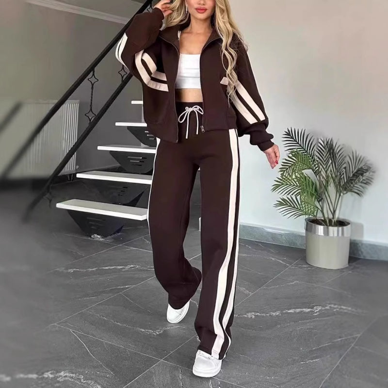 Femme marchant en ensemble marron foncé à bandes blanches, veste zippée et pantalon large à cordon blanc. 8