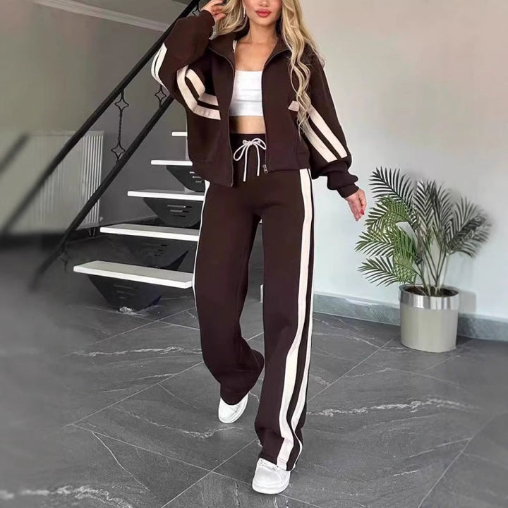 Femme marchant en ensemble marron foncé à bandes blanches, veste zippée et pantalon large à cordon blanc. 8