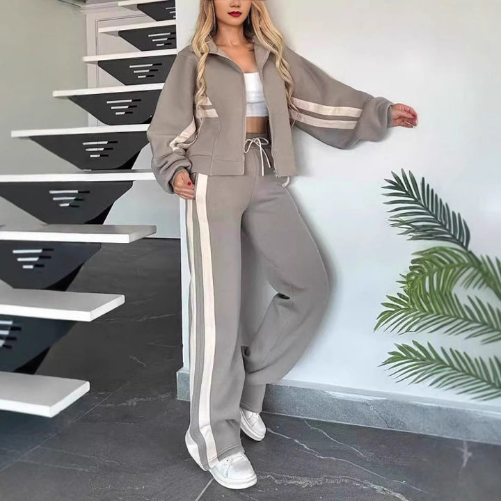 Femme adossée à un mur en ensemble gris à bandes beiges, veste zippée aux manches larges et pantalon large. 6