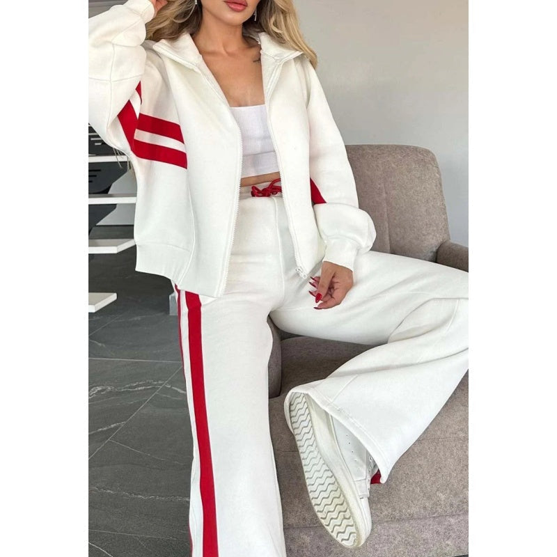 Gros plan sur le buste d'une femme assise, en veste blanche zippée à bandes rouges et pantalon large. 2