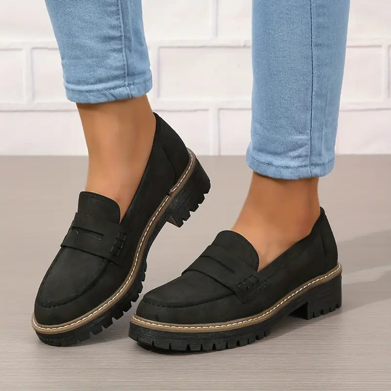 Mocassins noirs en daim portés avec un jean bleu retroussé, l'un des pieds légèrement relevé. 6