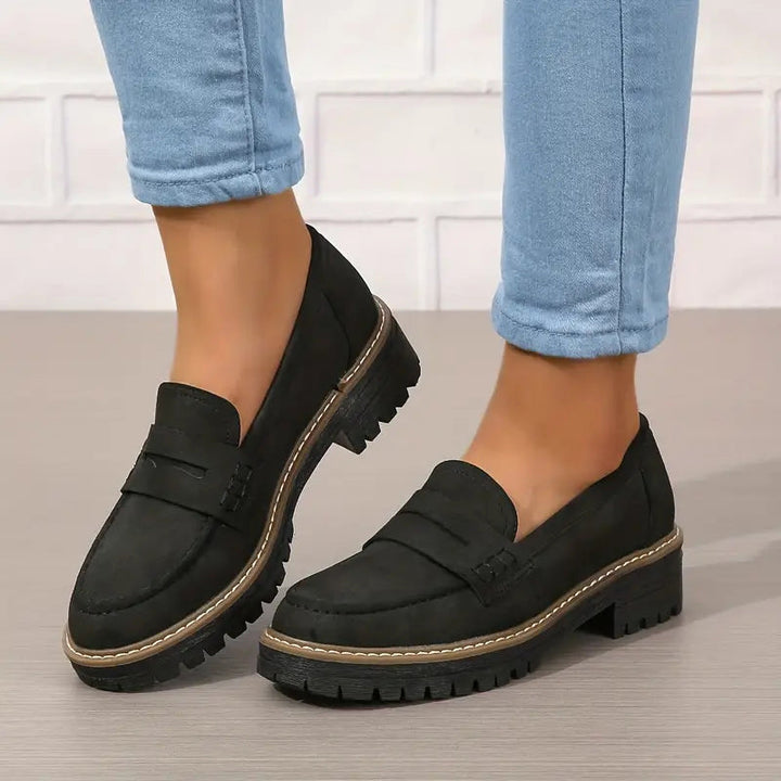 Mocassins noirs en daim portés avec un jean bleu retroussé, l'un des pieds légèrement relevé. 6