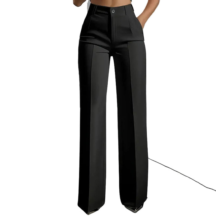 Vue de face du pantalon noir taille haute à jambe droite, pli marqué et fermeture à bouton, une main dans la poche. 1