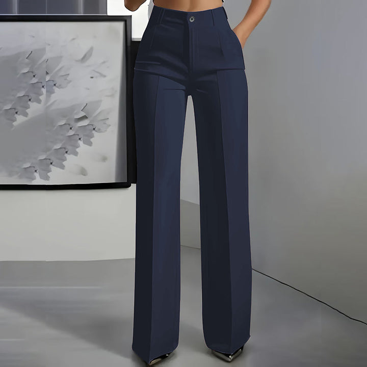 Vue de face du pantalon en bleu marine, porté taille haute avec pli sur chaque jambe, devant un tableau gris. 2