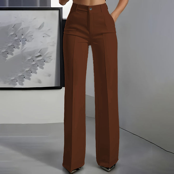 Vue de face du pantalon marron chocolat, taille haute, jambe droite et pli, porté devant un décor gris. 8