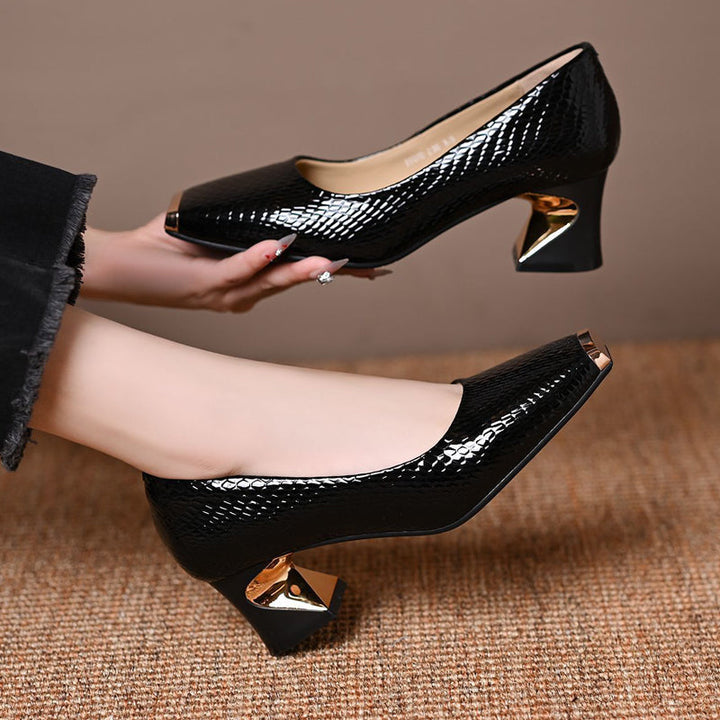 Escarpins noirs imprimé serpent, une paire portée et l'autre tenue en main, montrant le talon doré et l'intérieur beige. 5
