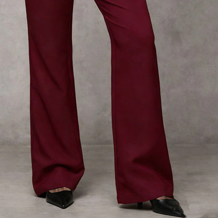Détail du bas de jambes évasées du pantalon bordeaux, porté avec des escarpins noirs pointus sur fond gris. 10