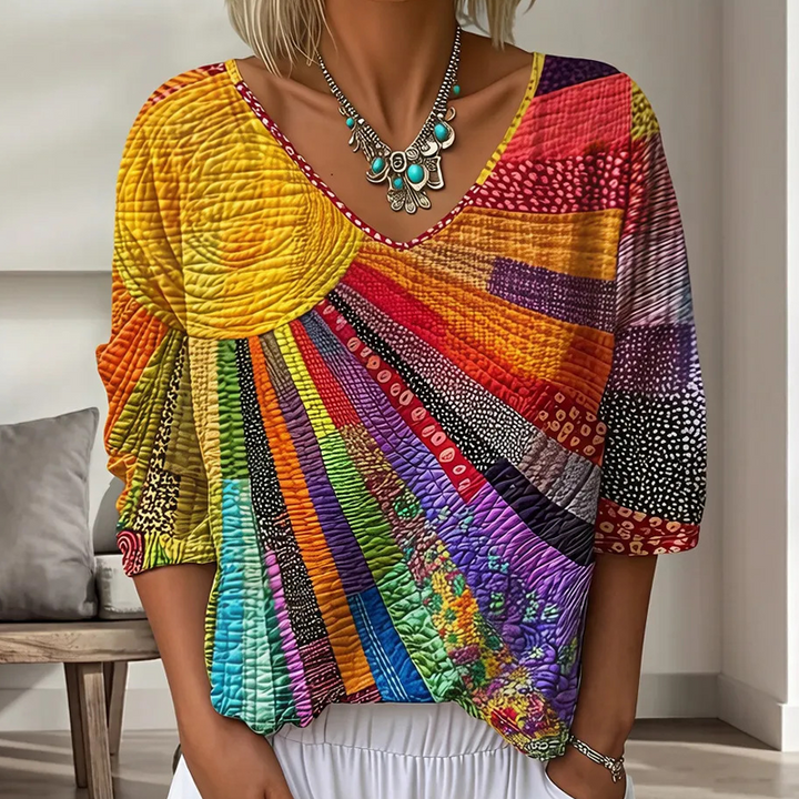 Buste de femme portant la blouse à col en V, patchwork de rayons en jaune, orange, rouge, violet et turquoise, avec un collier. 1