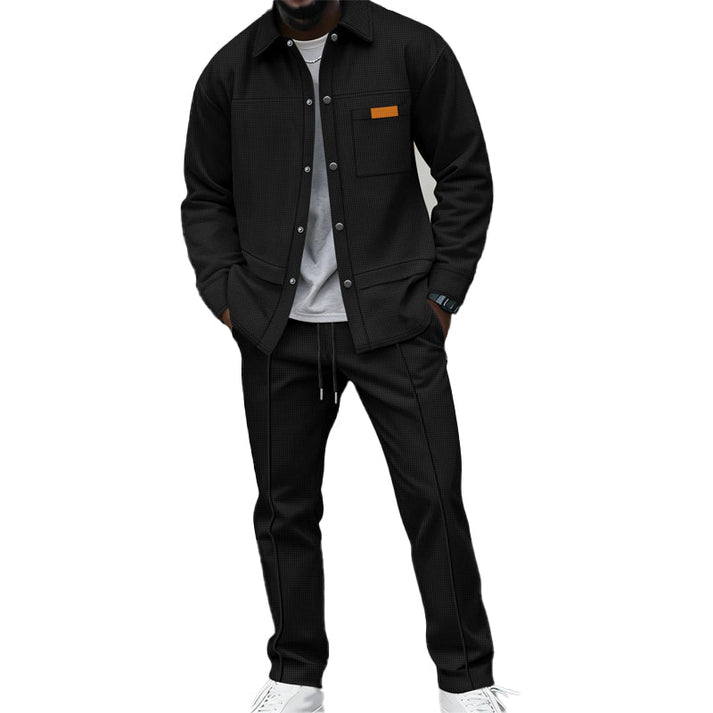 Homme portant l'ensemble noir, chemise boutonnée sur t-shirt gris, mains dans les poches, baskets blanches 1