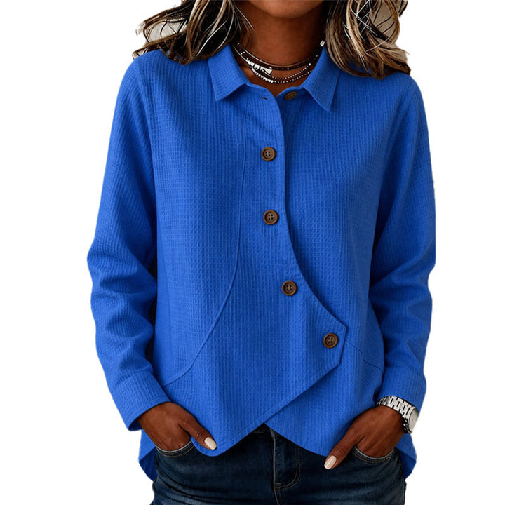 Femme portant le haut gaufré bleu roi à col chemise, boutons marron et ourlet asymétrique, mains dans les poches du jean. 1