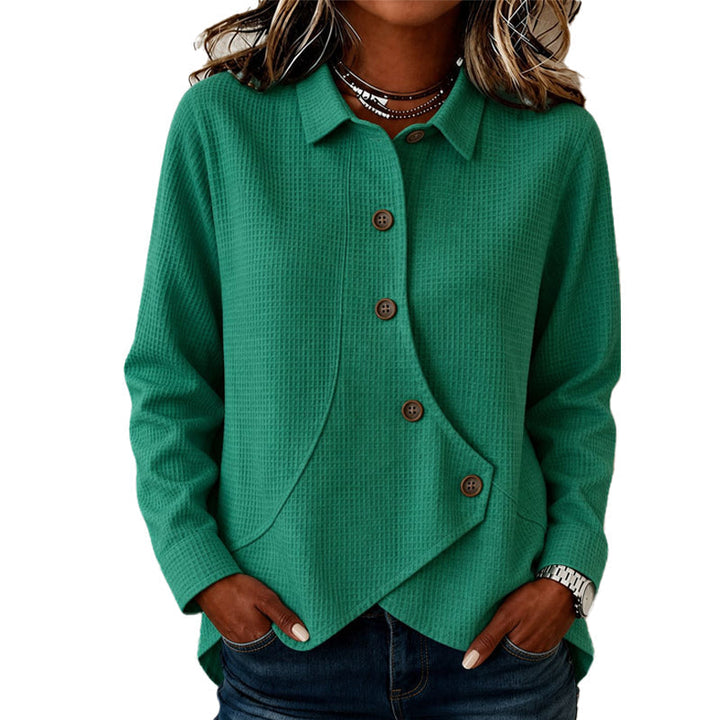 Pull vert en maille gaufrée porté par une femme, col chemise, patte de boutonnage asymétrique et boutons marron, mains dans les poches. 2