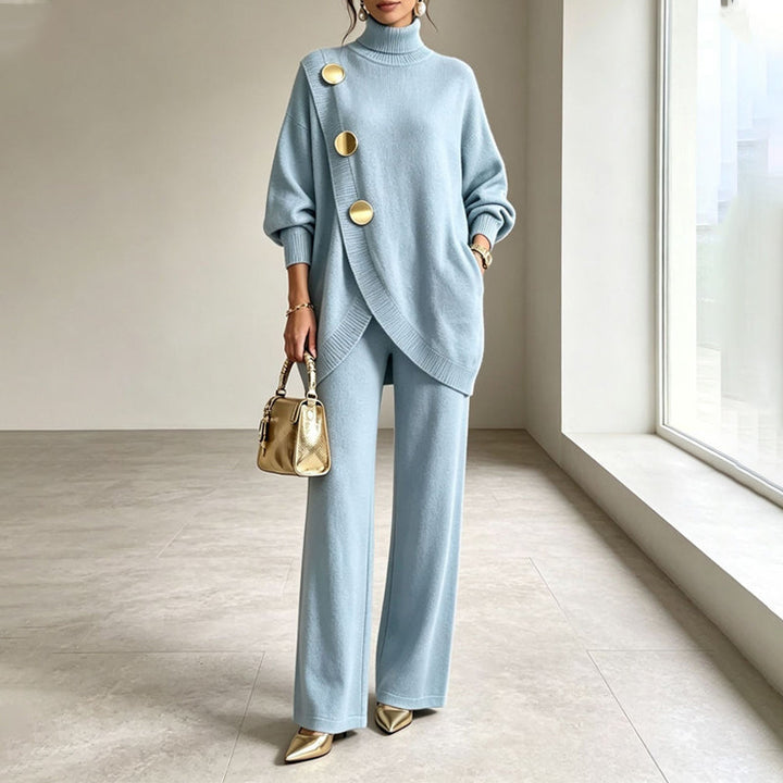 Ensemble en maille bleu clair porté par un mannequin, col roulé, boutons dorés en diagonale, sac doré à la main. 1