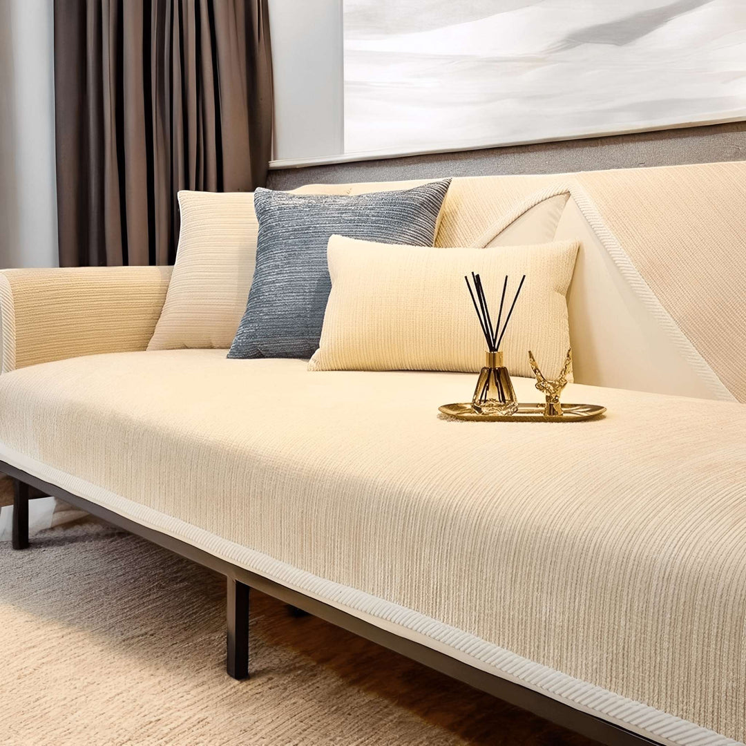 Housse crème à fines côtes sur un canapé, coussins crème et bleu-gris, diffuseur de parfum et plateau doré posés sur l'assise. 4