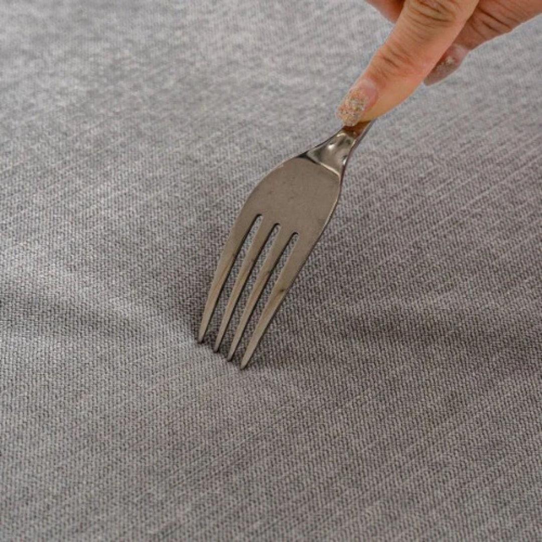 Fourchette tenue à la main contre le tissu gris serré de la housse, test de résistance aux rayures et accrocs. 11