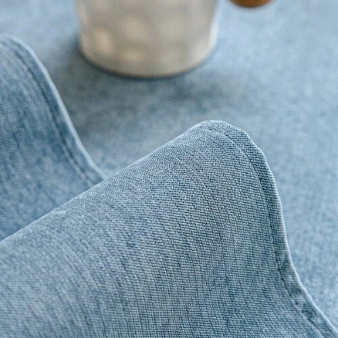 Gros plan sur le tissu bleu clair de la housse, finement tissé, avec couture du bord et tasse floue à l'arrière-plan. 8