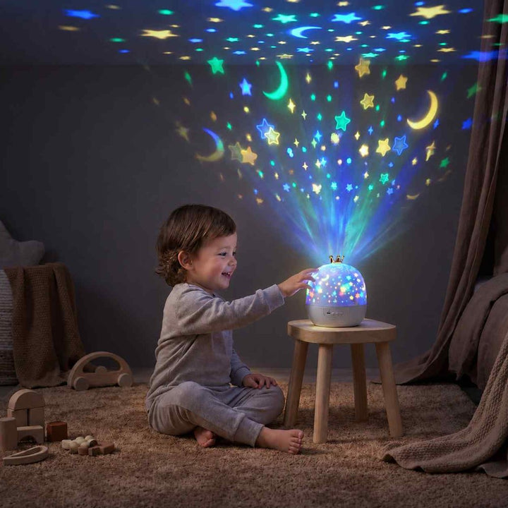 Tout-petit assis sur un tapis qui touche la veilleuse posée sur un tabouret, étoiles et lunes projetées au plafond 1