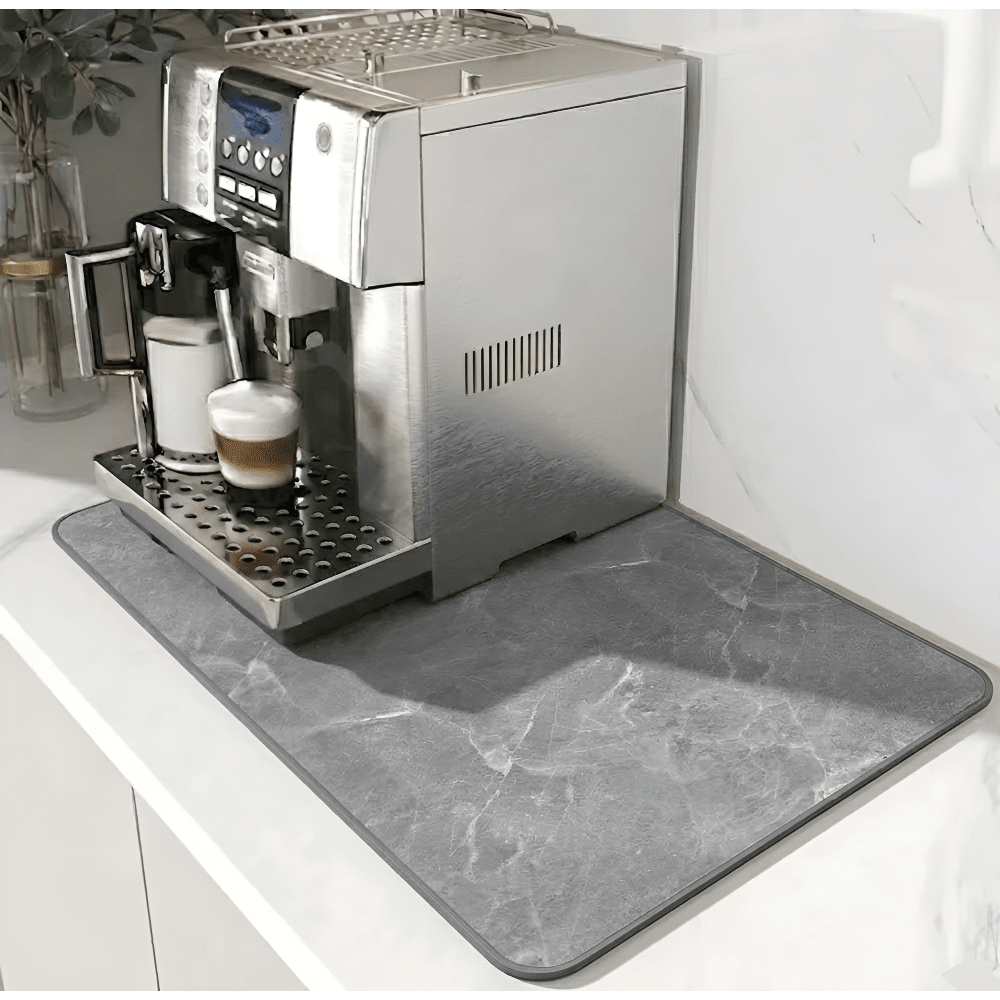 Tapis gris à motif marbré et bordure grise foncée, installé sous une machine à café sur un plan blanc. 12