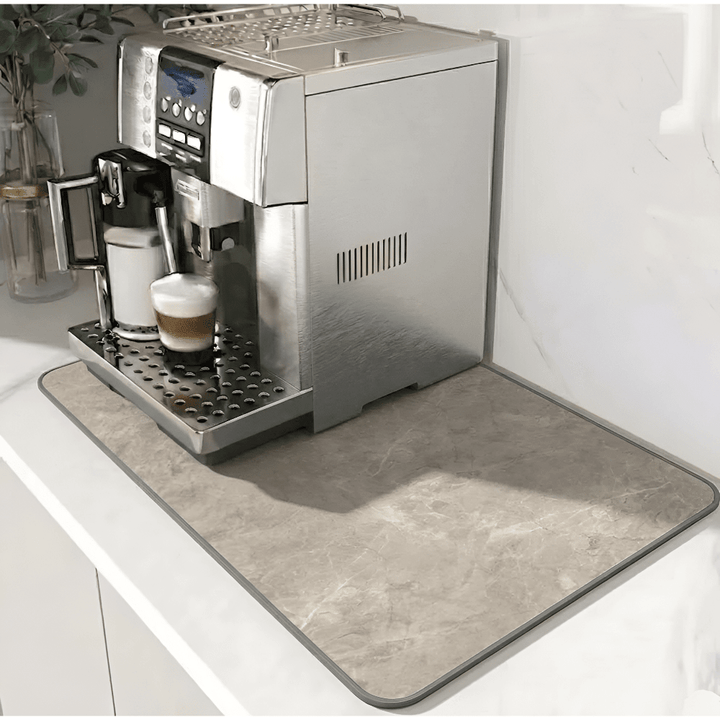 Tapis beige grisé à motif marbré et bordure grise, posé sous une machine à café en inox. 11
