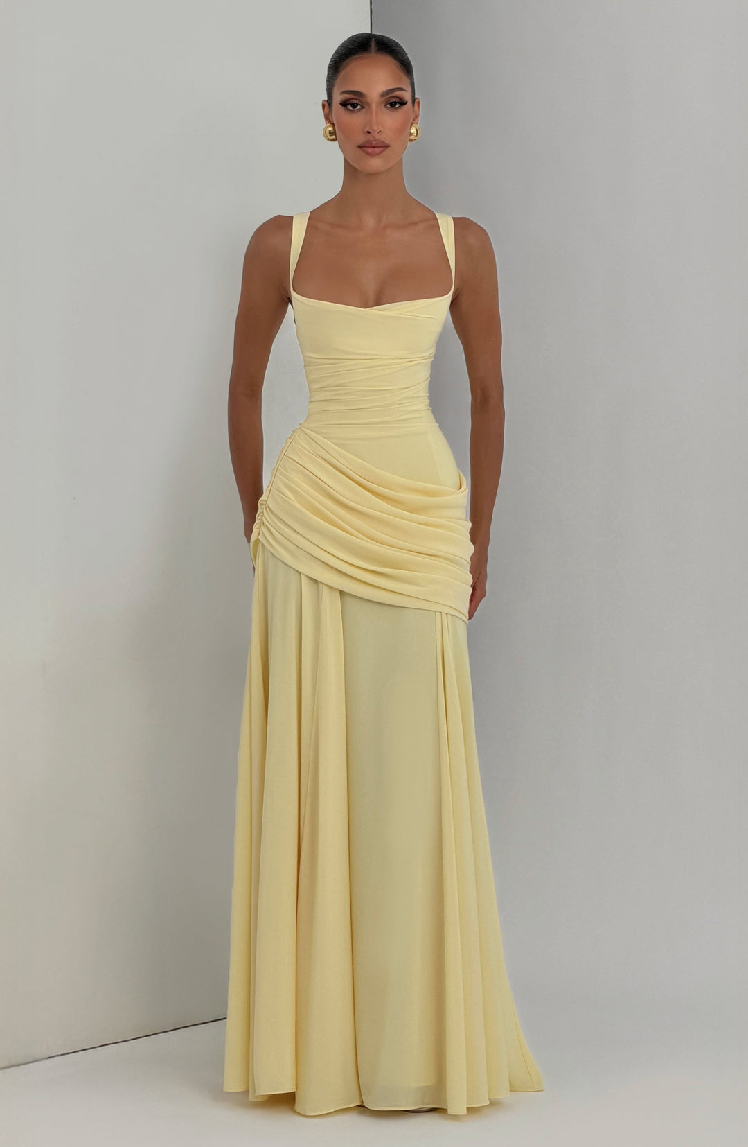 Robe longue jaune pâle portée de face devant un mur gris, jupe évasée et drapé asymétrique sur la hanche. 6