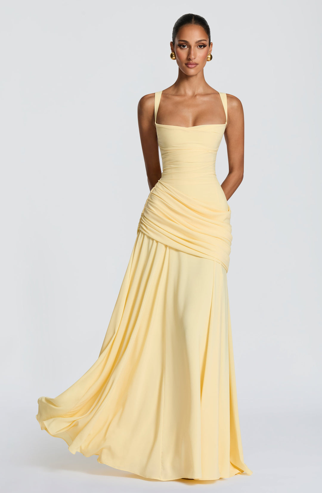 Mannequin vue de face portant la robe longue jaune pâle, jupe en mousseline qui virevolte, drapé en biais sur la hanche. 1