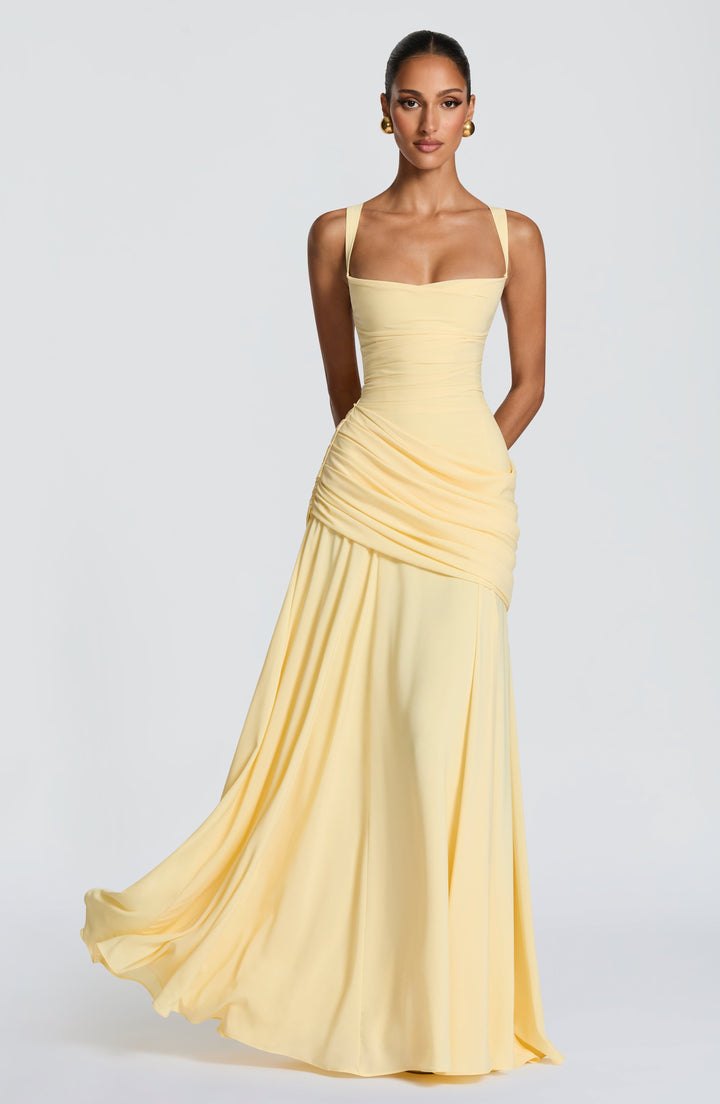 Mannequin vue de face portant la robe longue jaune pâle, jupe en mousseline qui virevolte, drapé en biais sur la hanche. 1