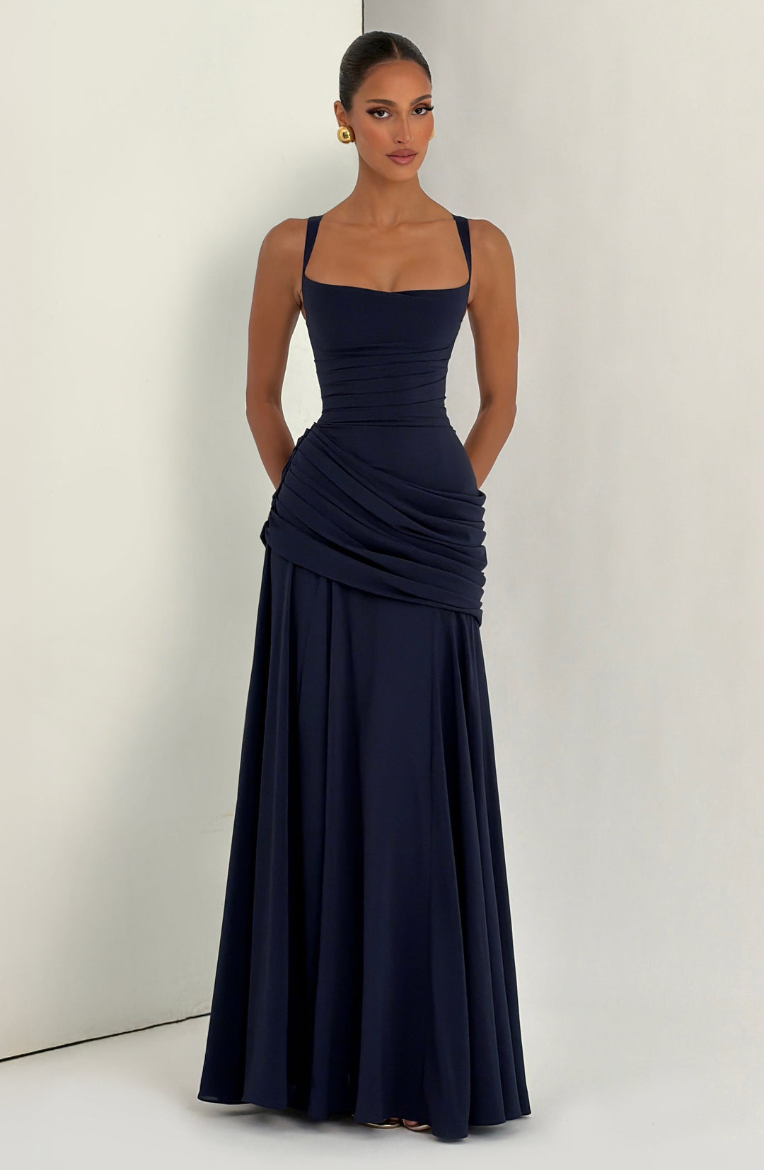 Robe bleu marine portée devant un fond de studio clair, mains le long du corps, drapé asymétrique et jupe fluide. 11