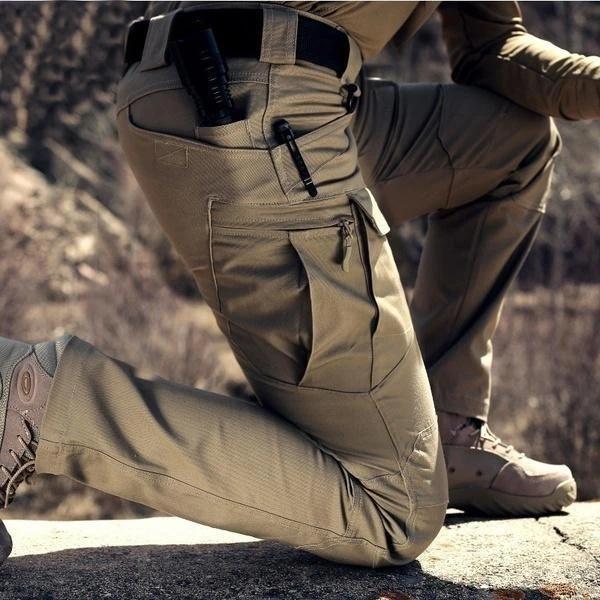 Homme agenouillé en extérieur, gros plan sur la poche cargo latérale zippée du pantalon beige 2